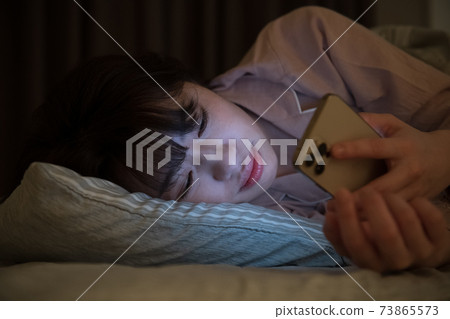 A woman looking at a room smartphone in a futon at night A woman looking at a room smartphone in a futon at night 73865573