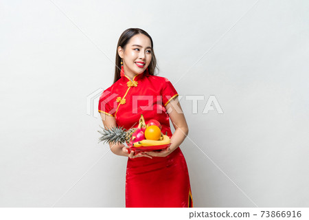 Young Asian woman in traditinal red cheongsam dress holding lucky fruits 73866916