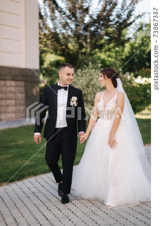 Beautiful bride with her handsome groom walking outside on theri wedding day. Happy newlyweds 73867387