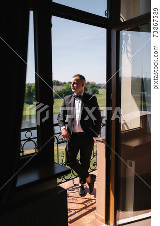 Groom stand in window by balcony at hotel. Handsome groom waiting for bride 73867589