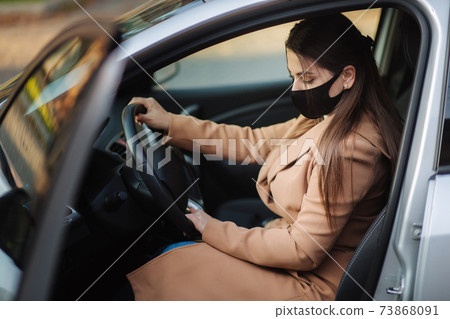 Beautiful young girl in a mask sitting in a car and put on protective gloves. Protective mask against covid-19, driver on a city street during a coronavirus outbreak Beautiful young girl in a mask sitting in a car and put on protective gloves. Protective mask against covid-19, driver on a city street during a coronavirus outbreak 73868091