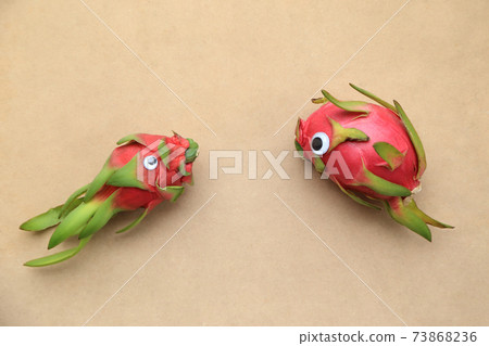 Minimal still life photography. A dragonfruit on brown paper background wearing doll's eyes. Minimal still life photography. A dragonfruit on brown paper background wearing doll's eyes. 73868236