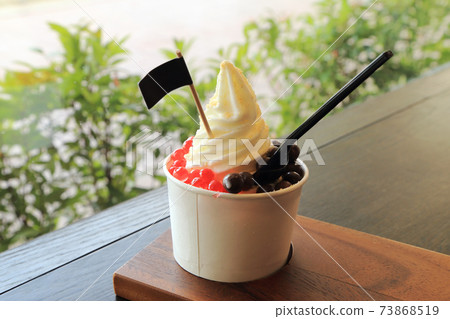 Milky ice cream soft serve in paper cup topping with chocolate ball and red jelly. Milky ice cream soft serve in paper cup topping with chocolate ball and red jelly. 73868519