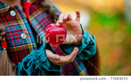 A girl holding a red apple in her hands in the autumn garden on a blurred background, place for text. 73869035