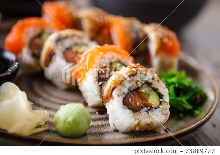 Sushi maki rolls with salmon, eel, avocado, cucumber on a plate with chopsticks, soy sauce, wasabi and ginger. Japanese traditional fish food closeup served for lunch in modern gourmet restaurant 73869727