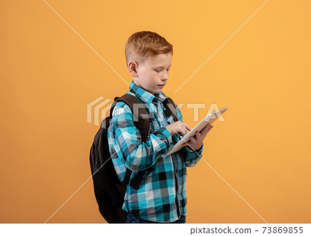 Ginger kid schooler using digital tablet on yellow Ginger kid schooler using digital tablet on yellow 73869855