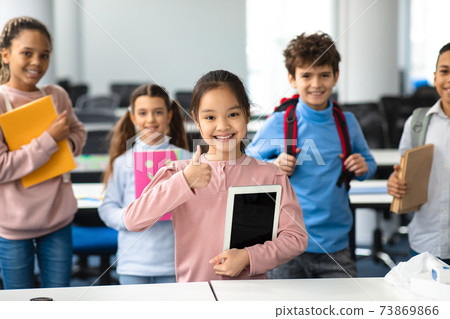Smiling asian girl holding tablet showing thumbs up gesture 73869866