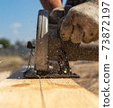 A worker cuts a wooden board at a construction site 73872197