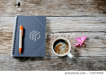 Black notebook with coffee cup and flower on old wooden table top view 73874400