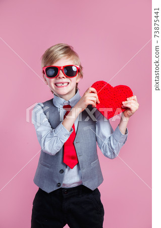Valentines day. Stylish little boy in red glasses posing with heart on pink background 73875441