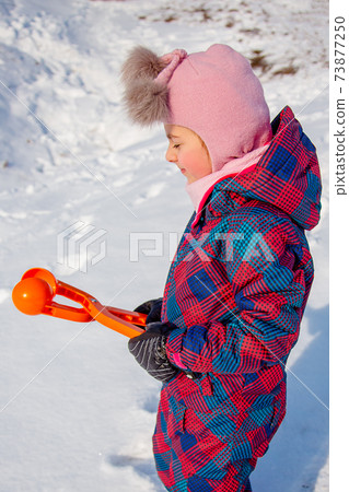 Happy girl playing with snow on a snowy winter walk, making snowballs in the park. Happy girl playing with snow on a snowy winter walk, making snowballs in the park. 73877250