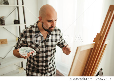 Artist at work. Young man doing easel drawing 73877807
