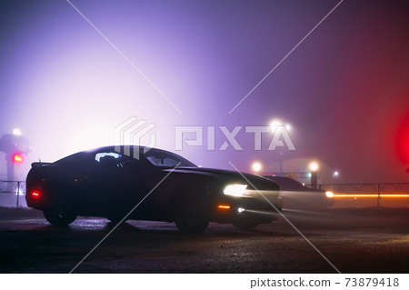 Sport car in the shadows with glowing lights in low light at foggy night, or silhouette of sport car dark background. Selective focus Sport car in the shadows with glowing lights in low light at foggy night, or silhouette of sport car dark background. Selective focus 73879418