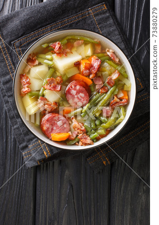 Bouneschlupp is a traditional Luxemburgish green bean soup with potatoes, bacon, and onions close-up in a plate. Vertical top view Bouneschlupp is a traditional Luxemburgish green bean soup with potatoes, bacon, and onions close-up in a plate. Vertical top view 73880279