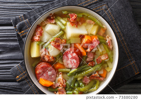 Luxembourgish soup of green beans, potatoes, leeks, carrots with the addition of sausages and bacon close-up in a plate. Horizontal top view 73880280