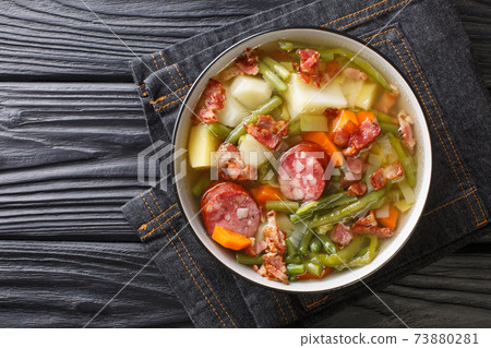 Homemade soup of green beans, potatoes, leeks, carrots with sausages and bacon close-up on a plate. Horizontal top view 73880281