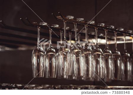 raws of glasses for a margarita, martini, grog and liqueur hanging upside down in bar at arestaurant, dark background. 73880348