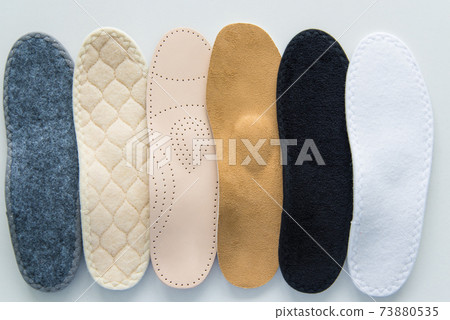 Studio photo of orthopedic insoles. A variety of orthopedic insoles are laid out in a row. Different colors and coatings: leather, cotton, microfiber. 73880535