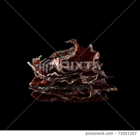 Dried deer meat. Nutritional snack stacked with thin curly plates pyramid tongues, isolated on a black background. Dried deer meat. Nutritional snack stacked with thin curly plates pyramid tongues, isolated on a black background. 73881307