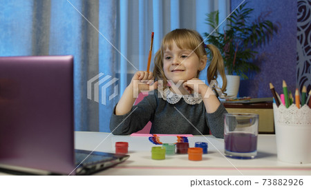 Kid pupil girl artist sitting and painting on paper, drawing coloring picture rainbow with paints Kid pupil girl artist sitting and painting on paper, drawing coloring picture rainbow with paints 73882926