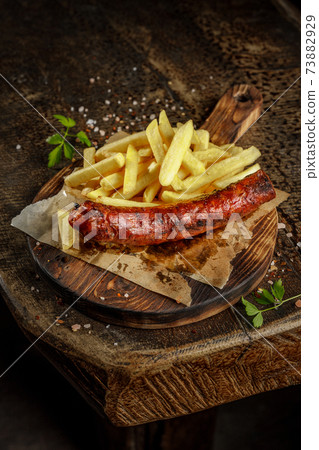 Grill house concept. Grilled, roasted tasty sausage with french fries on the old wooden cutting board. Grill house concept. Grilled, roasted tasty sausage with french fries on the old wooden cutting board. 73882929
