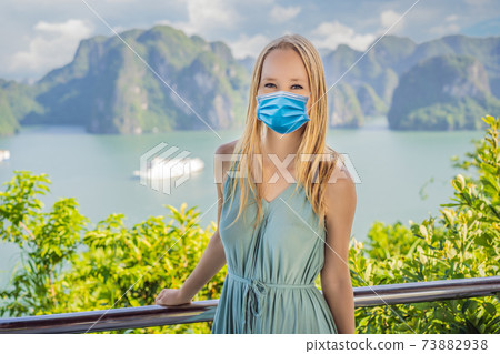 Attractive woman in a dress wearing a medical mask during COVID-19 coronavirus is traveling in Halong Bay. Vietnam. Travel to Asia, happiness emotion, summer holiday concept. Picturesque sea landscape 73882938
