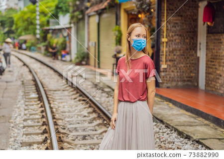Woman wearing a medical mask during COVID-19 coronavirus is walking of Hanoi city railway. Perspective view running along narrow street with houses in Vietnam. Hanoi train street, old house and Woman wearing a medical mask during COVID-19 coronavirus is walking of Hanoi city railway. Perspective view running along narrow street with houses in Vietnam. Hanoi train street, old house and 73882990
