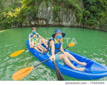 Mom, dad and son travelers wearing a medical mask during COVID-19 coronavirus rowing on a kayak in Halong Bay. Vietnam. Travel to Asia, happiness emotion, summer holiday concept. Traveling with 73883004