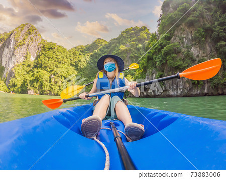 Mom, dad and son travelers wearing a medical mask during COVID-19 coronavirus rowing on a kayak in Halong Bay. Vietnam. Travel to Asia, happiness emotion, summer holiday concept. Traveling with Mom, dad and son travelers wearing a medical mask during COVID-19 coronavirus rowing on a kayak in Halong Bay. Vietnam. Travel to Asia, happiness emotion, summer holiday concept. Traveling with 73883006
