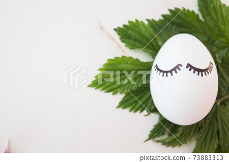 Minimal easter concept white egg and tropical branches with leaves. Stylish Easter white egg on a marble background. The flat lay fashionable easter. Happy easter card with copy space for text 73883313