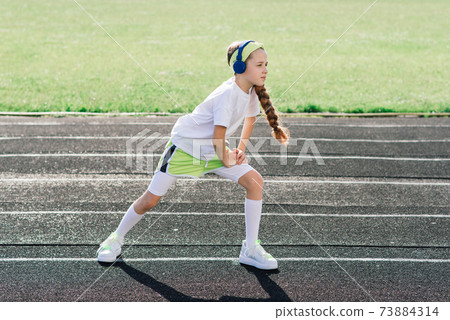Girl jogging on a sunny summer evening, laying on treadmill, stadium, physical training, back to school. 73884314