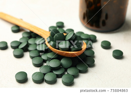 Bottle and wooden spoon with spirulina pills on white textured background Bottle and wooden spoon with spirulina pills on white textured background 73884863