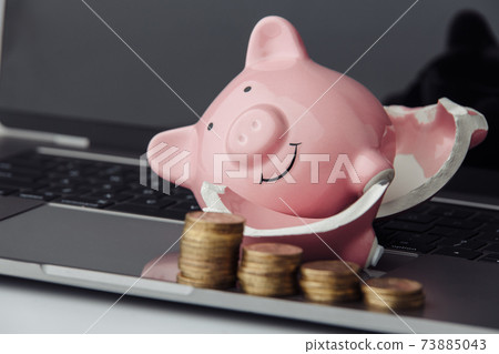 Broken pink piggy bank and stack of coins on a laptop close-up 73885043