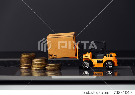 Mini model of forklift with carton boxes snd coins on keyboard close-up. Logistics and delivery concept 73885049