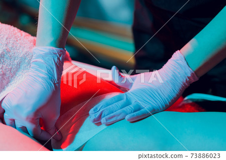 Mid section of therapist waxing woman's leg at spa center. 73886023