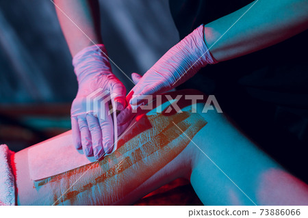 Mid section of therapist waxing woman's leg at spa center. 73886066