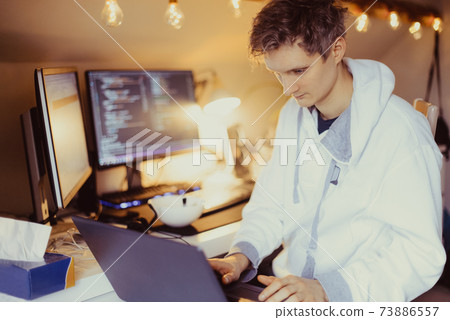 A man sitting at a desk working from home on his computer. IT specialist programmer writing code on his pc and laptop. Developer remote home office. Freelance workspace. Soft selective focus 73886557