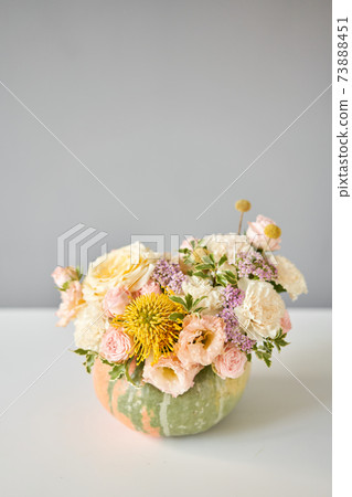 Flowers arrangement in pumpkin on the white table. Fresh cut flowers for decoration home. European floral shop. Delivery fresh cut flower. 73888451