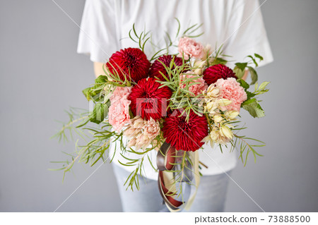 Red tones Beautiful bouquet of mixed flowers in womans hands. the work of the florist at a flower shop. Handsome fresh bouquet. Flowers delivery 73888500