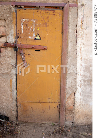 Locked old rusty yellow door with high voltage sign. Transformer substation, closed padlock 73889477