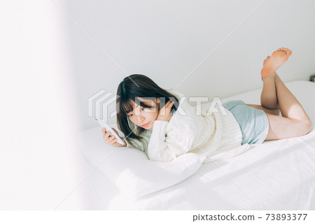 A girl lying on the bed and looking at her smartphone A girl lying on the bed and looking at her smartphone 73893377