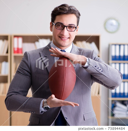 Businessman with american football in office Businessman with american football in office 73894484