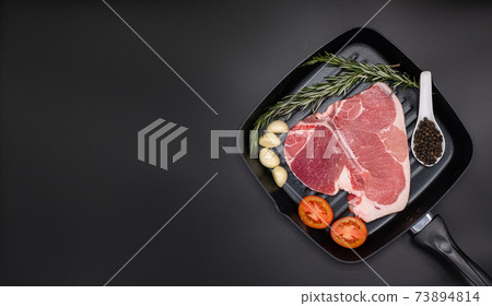 Raw T-bone Steak with fresh herbs and garlic, tomato, black pepper, rosemary on dark black background with copy space for your design, food concept. Top view. 73894814