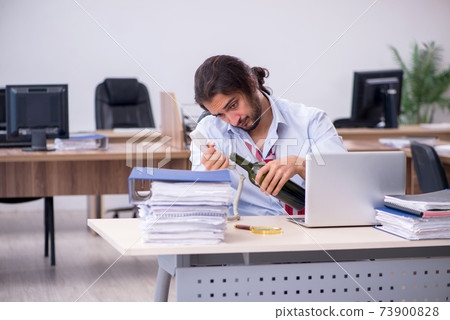 Young male employee drinking alcohol in the office Young male employee drinking alcohol in the office 73900828