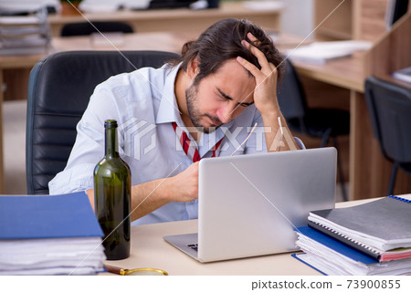 Young male employee drinking alcohol in the office Young male employee drinking alcohol in the office 73900855