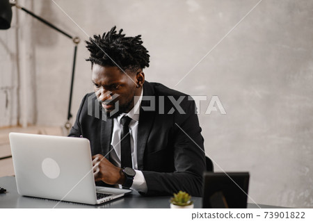Handsome african american businessman in classic suit uses laptop and smiles while working in office 73901822