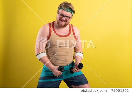 Funny fat man in sportswear with dumbbells in his hands. Overweight man goes in for sports. Yellow background isolate Funny fat man in sportswear with dumbbells in his hands. Overweight man goes in for sports. Yellow background isolate 73901861