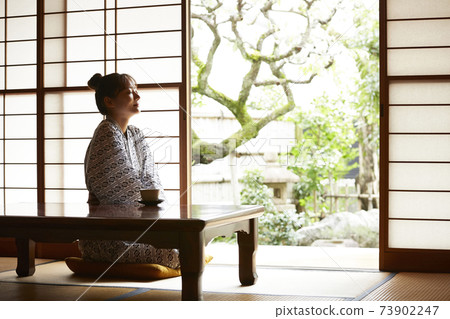 一個年輕的女人，穿著浴衣放鬆在一家旅館 73902247