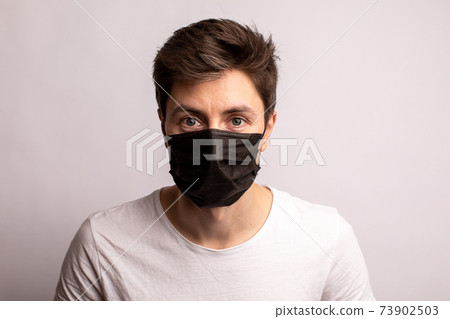 studio shot of a young man wearing a black mask, looking at camera, isolated on white background 73902503