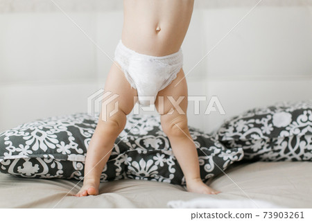 small child in a diaper. baby in diaper standing on bed small child in a diaper. baby in diaper standing on bed 73903261